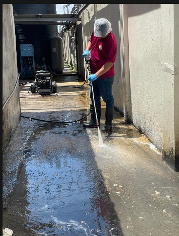 Crew member pressure washing a concrete service corridor at a production facility